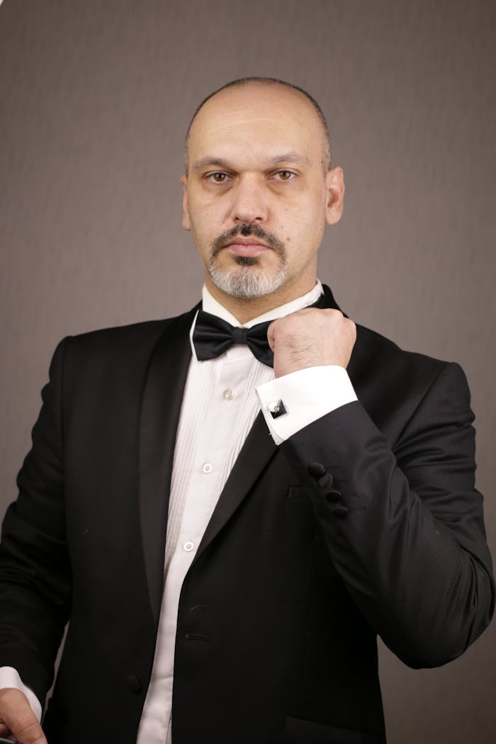 Stylish portrait of a man in a tuxedo adjusting his cufflinks, showcasing elegance.
